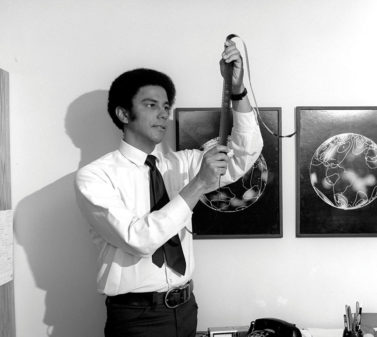 Vintage black and white picture of Warren Washington holding film in office