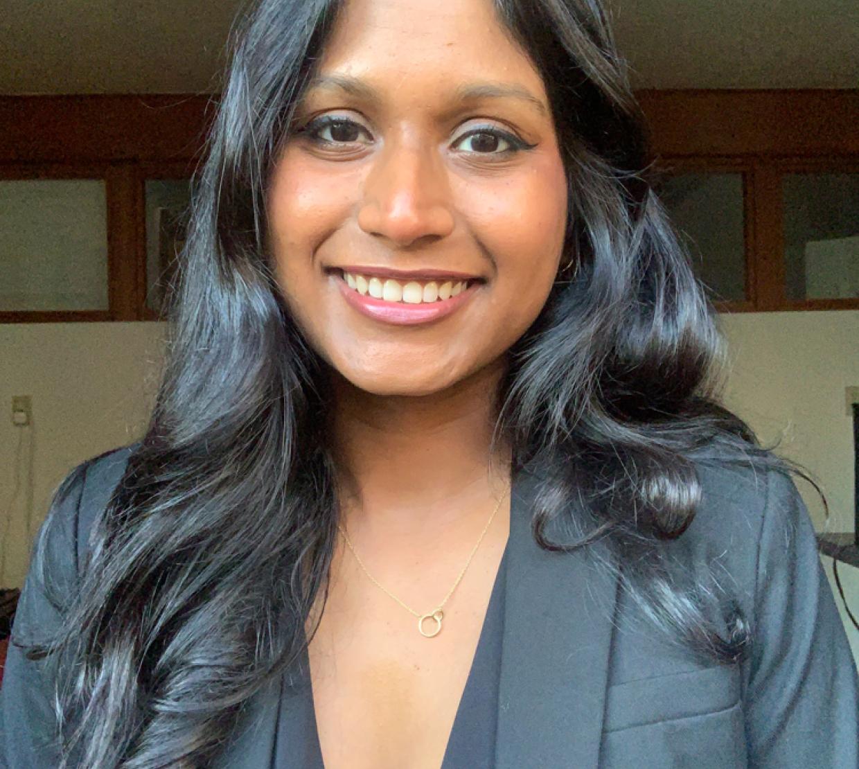 A smiling headshot of Sanjana Curtis in a blazer