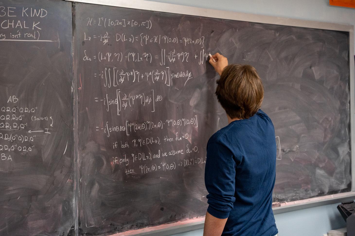 Takach fills a chalkboard with mathematical equations, with his back faced to the camera.