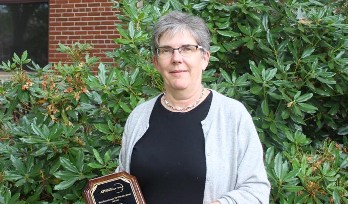 Heidi Schellman holding award in front of shrubbery